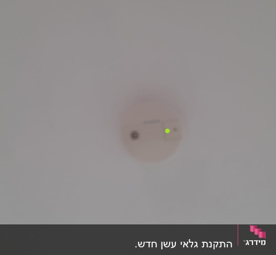 גלאי אש ועשן מותקן על תקרה עם נורית חיווי ירוקה פועלת